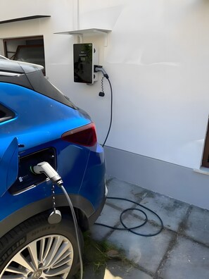 A blue car charging at a station with a visible cable and a power box. - Reginella Garden View Studio with Shared Terrace, Wi-Fi, and Air Conditioning (Meta)