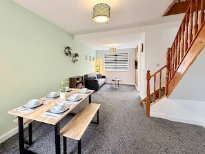 A dining area with a wooden table set for four, a sofa, a small side table, and a staircase. - Ward House - Contractors or Family Holidays (North East Lincolnshire)