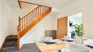 Ein Essbereich mit einer Holztreppe, einem gedeckten Esstisch mit Tellern, Schüsseln und Gläsern sowie einem Blumentopf.