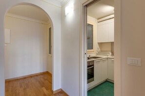 Un corridoio stretto che conduce a una cucina con mobili bianchi, una finestra e un tappeto verde.