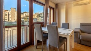 Ein Essbereich mit Tisch und Stühlen, große Fenster mit Blick auf Gebäude und einen Fluss, sowie eine Klimaanlage an der Wand.