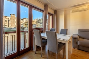 A dining area with a table and chairs, large windows with a view of buildings and a river, and an air conditioning unit on the wall. - Stunning Apartment with a View of the Ponte Vecchio (Florence)