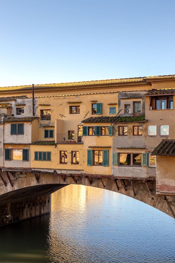 A multi-story building with balconies and windows, a bridge, and a calm water body below. - Stunning Apartment with a View of the Ponte Vecchio (Florence)