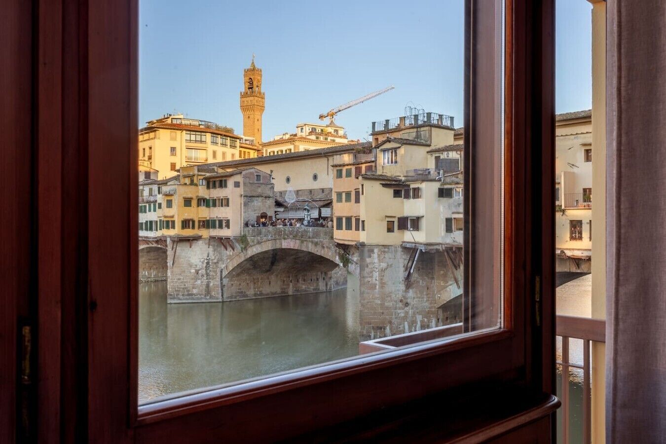 Blick durch ein Fenster auf eine historische Brücke über dem Wasser, mit Gebäuden und einem Turm im Hintergrund.
