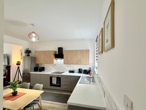 A modern kitchen with wooden cabinets, a stainless steel refrigerator, a microwave, and a built-in oven. - Lovett House - Contractors or Family Holidays (North East Lincolnshire)
