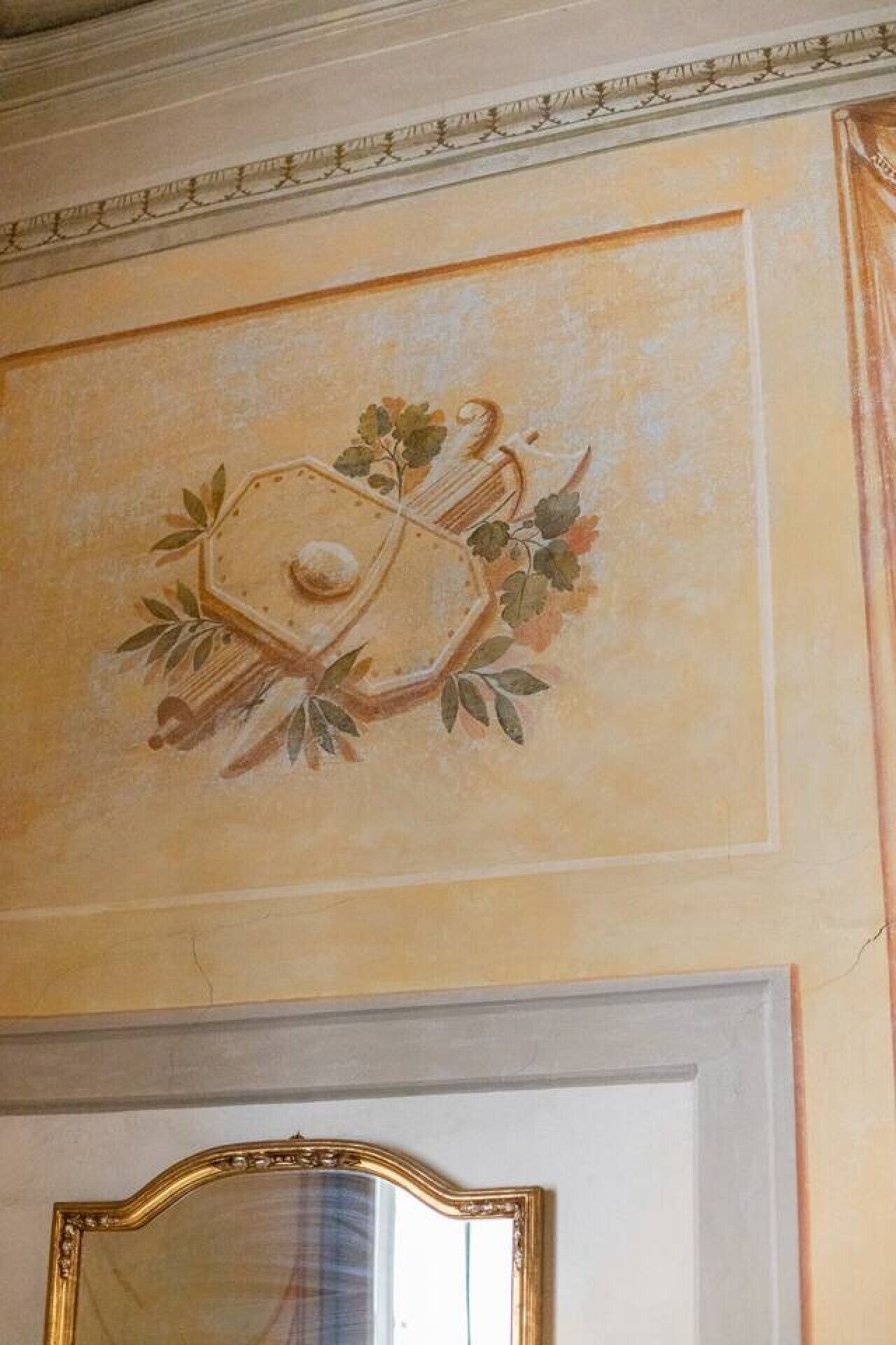 Een plafond met een decoratieve fresco, een witte deur met gouden lijst en een wand met decoratieve kroonlijst.