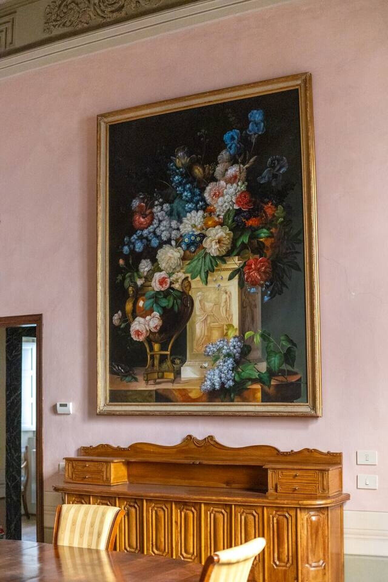 Een eetgedeelte met een groot bloemschilderij, een houten tafel en stoelen.