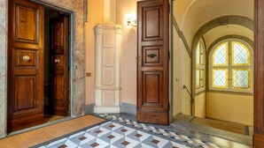 Un couloir avec des portes en bois, une colonne blanche, un sol à motifs et une fenêtre avec un cadre jaune.