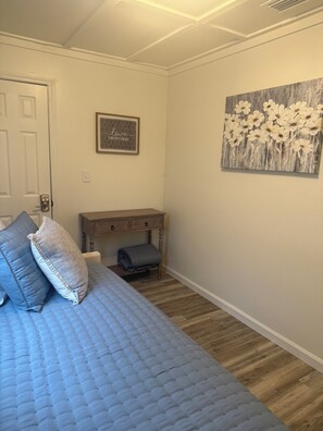 Een slaapkamer met een bed, een houten nachtkastje, een bureau en een muur met een bloemschilderij.
