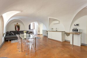 Ein großzügiges Loft mit Essbereich, Küche und Wohnbereich, das durch gewölbte Decken und ein großes Fenster gekennzeichnet ist.