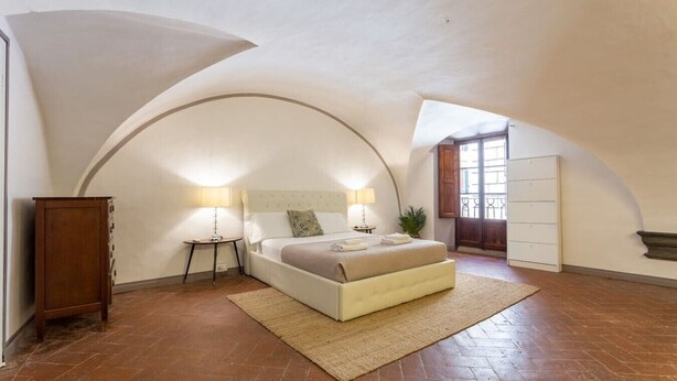 Een slaapkamer met een bed, twee nachtkastjes, een nachtkastje, een houten kast en een groot rondboogvenster.