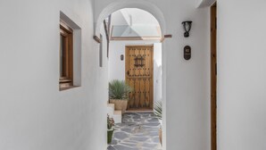 Un pasillo estrecho con una puerta de madera, suelo de piedra y una planta en maceta.
