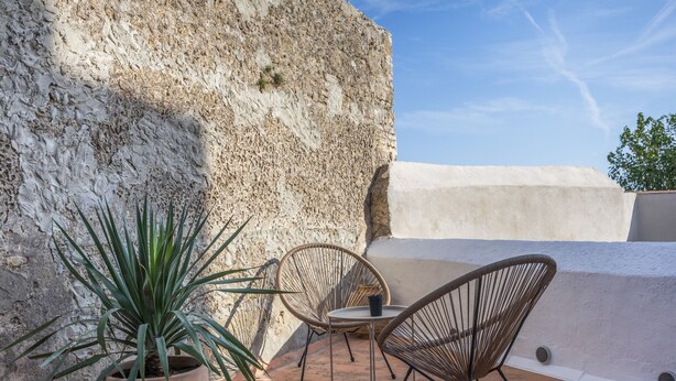 Un patio con planta en maceta, sillas de mimbre y una mesa.