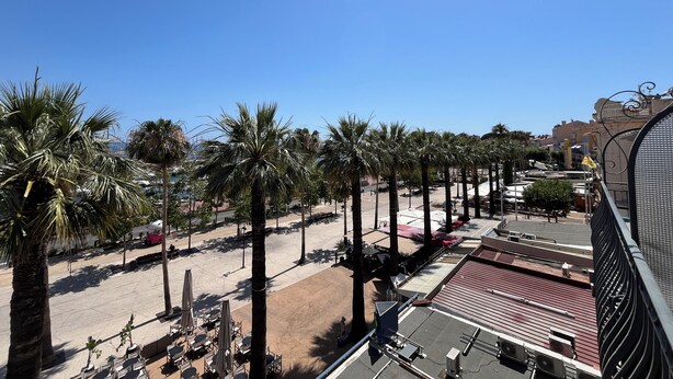 Una terraza en la azotea con palmeras, mobiliario exterior y vistas a la ciudad.