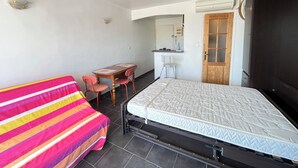 Una habitación con cama, escritorio, silla, kitchenette pequeña y una puerta.