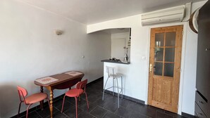 Habitación compacta con mesa de comedor, sillas, una pequeña barra y unidad de aire acondicionado. Puerta de madera.