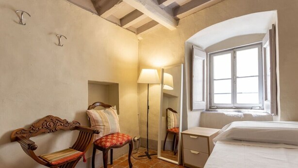 A room with a bed, a chair with a cushion, a floor lamp, a mirror, and a window. - Single Room in a Historic Building (Florence)