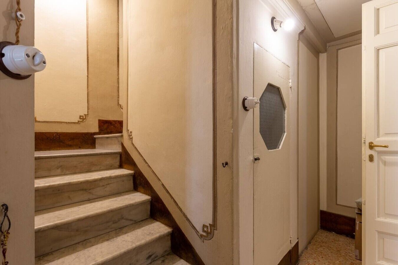 A hallway with marble stairs, a white door with a glass panel, and a brass door handle.