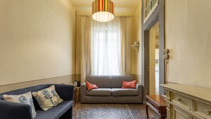 A room with a sofa, a small table, a cabinet, and a window with curtains. - Single Room in a Historic Building (Florence)