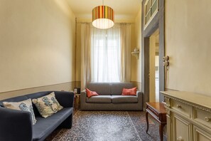 A room with a sofa, a small table, a cabinet, and a window with curtains. - Single Room in a Historic Building (Florence)