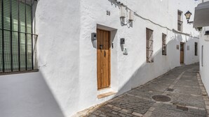 A narrow cobblestone street flanked by white buildings with wooden doors and windows, a number '20' sign, and a small step leading to the entrance. - Apartment '2' with Shared Terrace and Wi-Fi (Vejer de la Frontera)