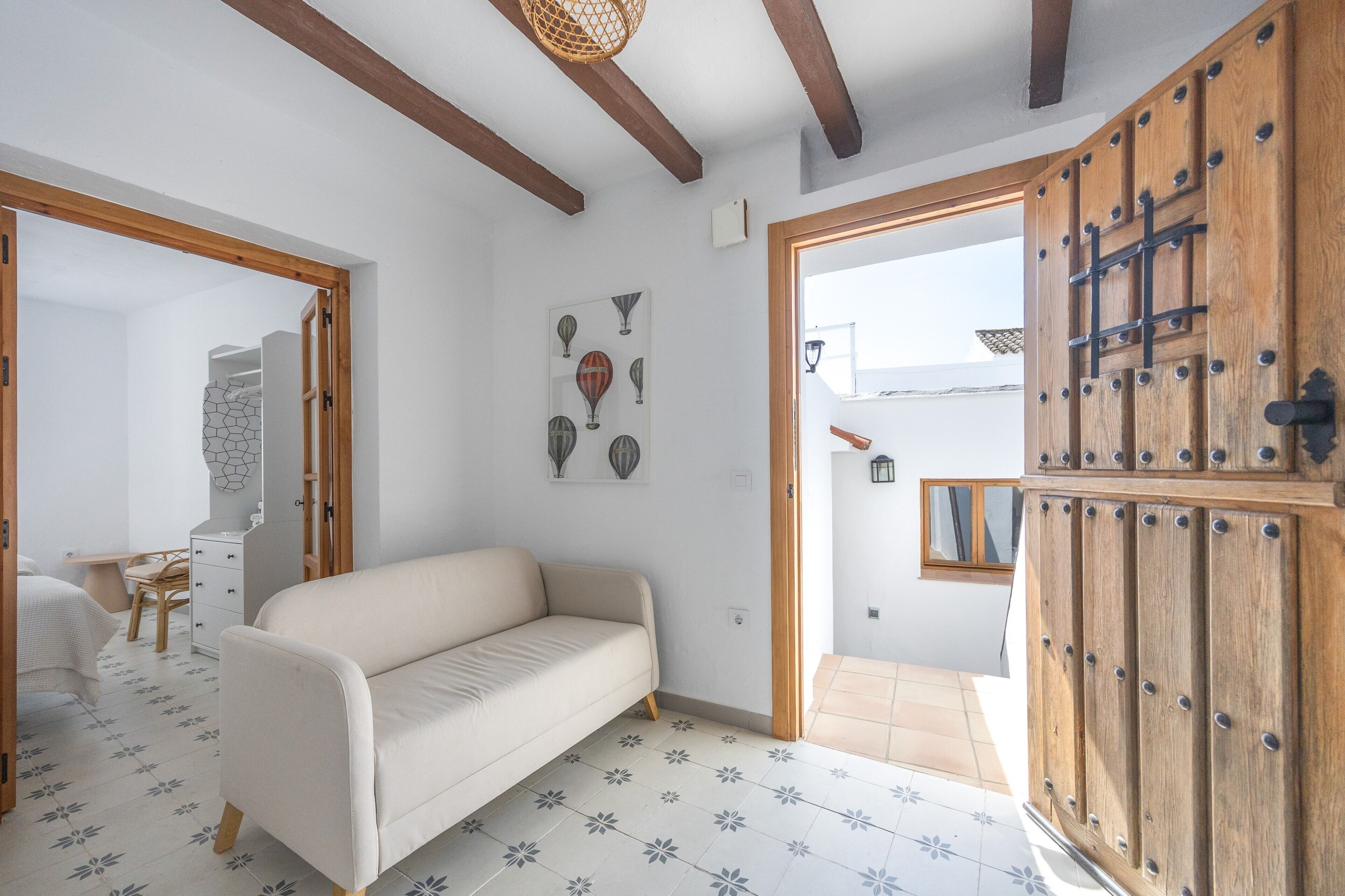 Una habitación con un sofá, una puerta de madera, suelo de baldosas y una pared con un cuadro enmarcado.