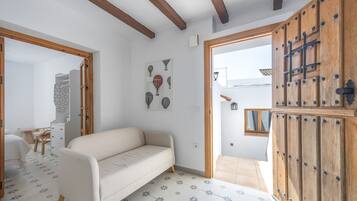Una habitación con un sofá, una puerta de madera, suelo de baldosas y una pared con un cuadro enmarcado.