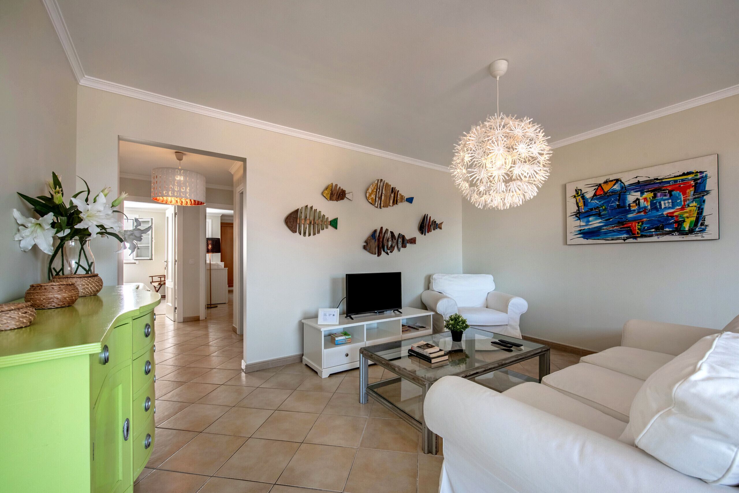 Un salon comprenant un canapé, une table basse, un téléviseur, une décoration murale représentant des poissons et un tableau.