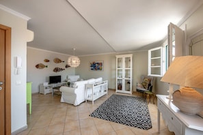 Ein Wohnzimmer mit einer Couch, Fernseher, weißem Schrank, Teppich mit Muster und Kunstwerken an der Wand.