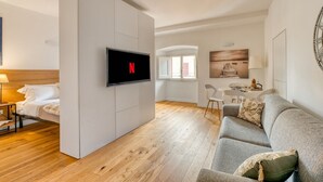 Un soggiorno moderno con una televisione a schermo piatto, un divano grigio, un pavimento in legno e un'area pranzo sullo sfondo.
