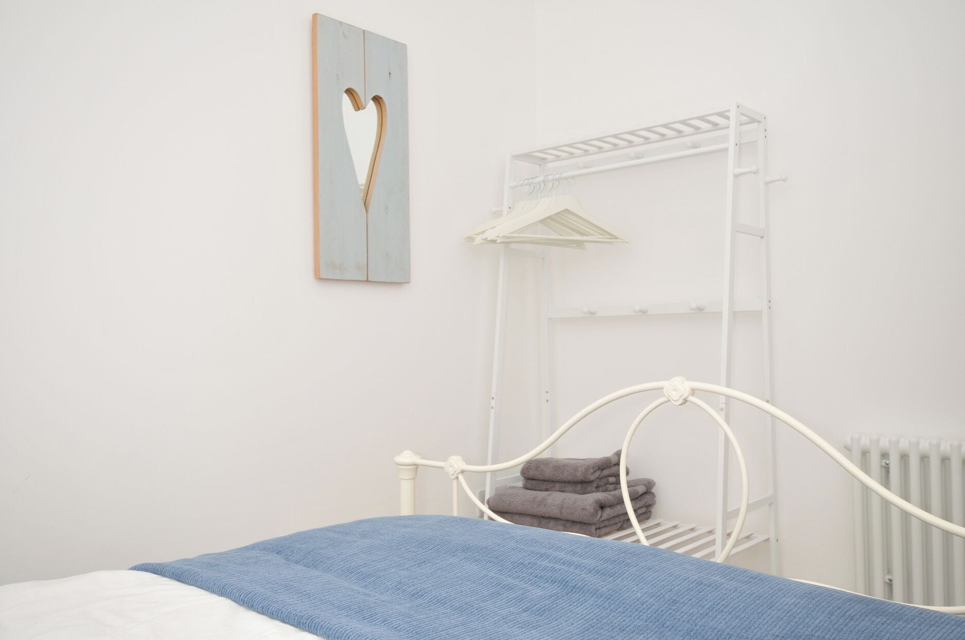 Un dormitorio con una cama, cabecera de metal blanco, estante de pared con toallas y un cuadro.