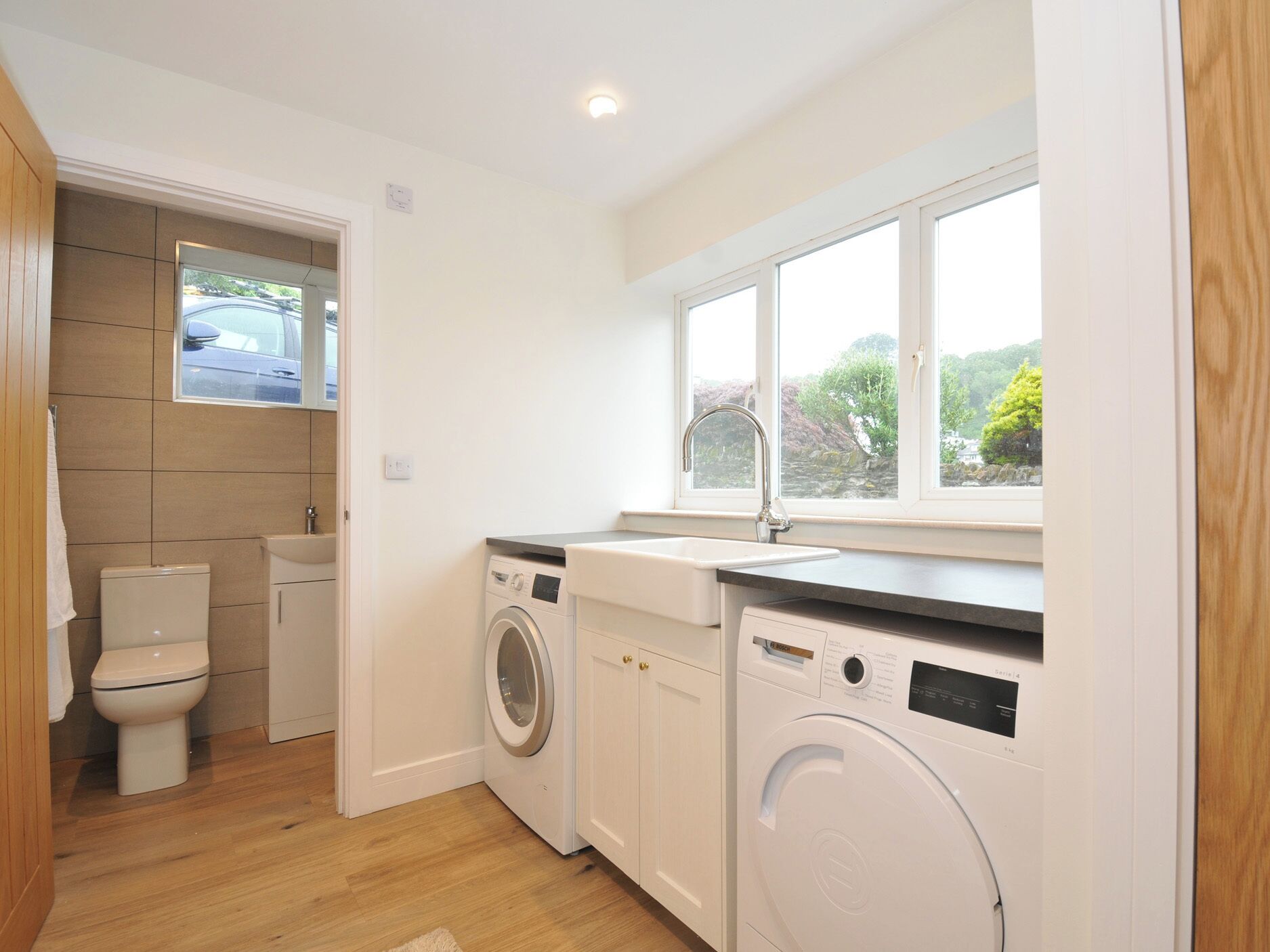 A compact kitchen with a washing machine, a sink, and a window with a view of greenery.