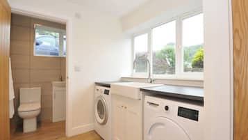 A compact kitchen with a washing machine, a sink, and a window with a view of greenery.