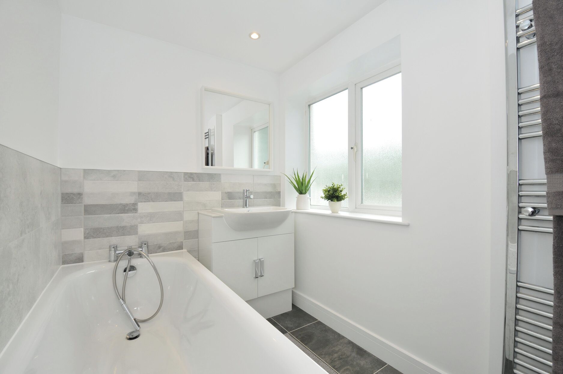 Un baño moderno con una bañera independiente, un tocador con espejo y una ventana con plantas.