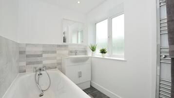 Un baño moderno con una bañera independiente, un tocador con espejo y una ventana con plantas.