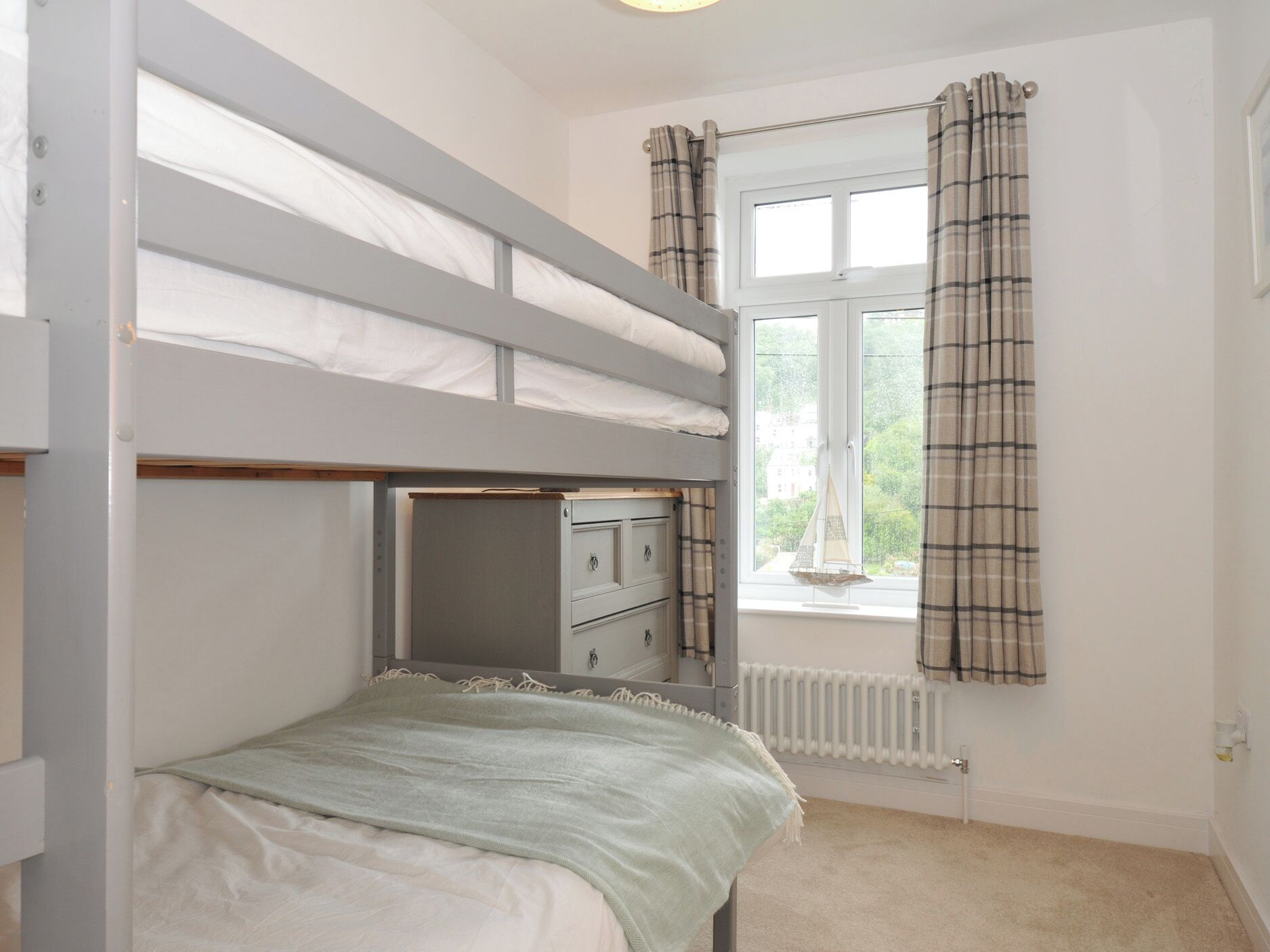 A bunk bed with a desk underneath, a window with curtains, and a radiator.