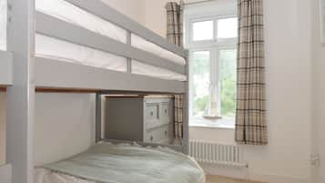 A bunk bed with a desk underneath, a window with curtains, and a radiator.