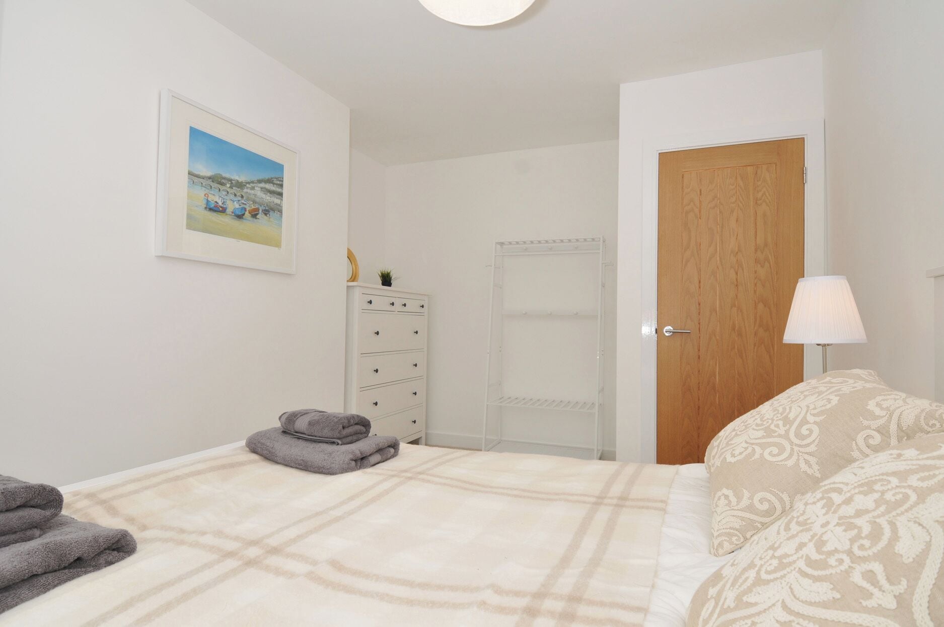 A bedroom with a bed, a dresser, a door, a lamp, and a framed picture on the wall.