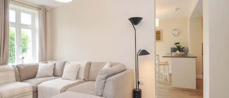 A modern living room with a sectional sofa, a floor lamp, and a view into the kitchen area.