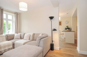 Een moderne woonkamer met een hoekbank, een vloerlamp en uitzicht op de keuken.