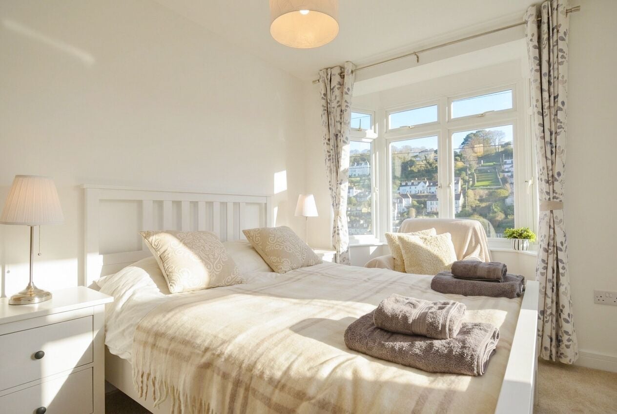A bedroom with a bed, bedside tables, a lamp, a window with curtains, and a view of the outside.
