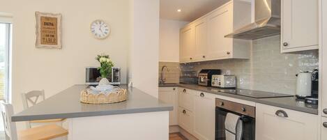 A modern kitchen with white cabinets, a built-in oven, and a central island with stools.