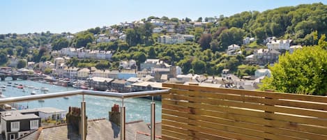 Une ville côtière avec vue sur la mer, des maisons construites sur une colline et une clôture en bois au premier plan.