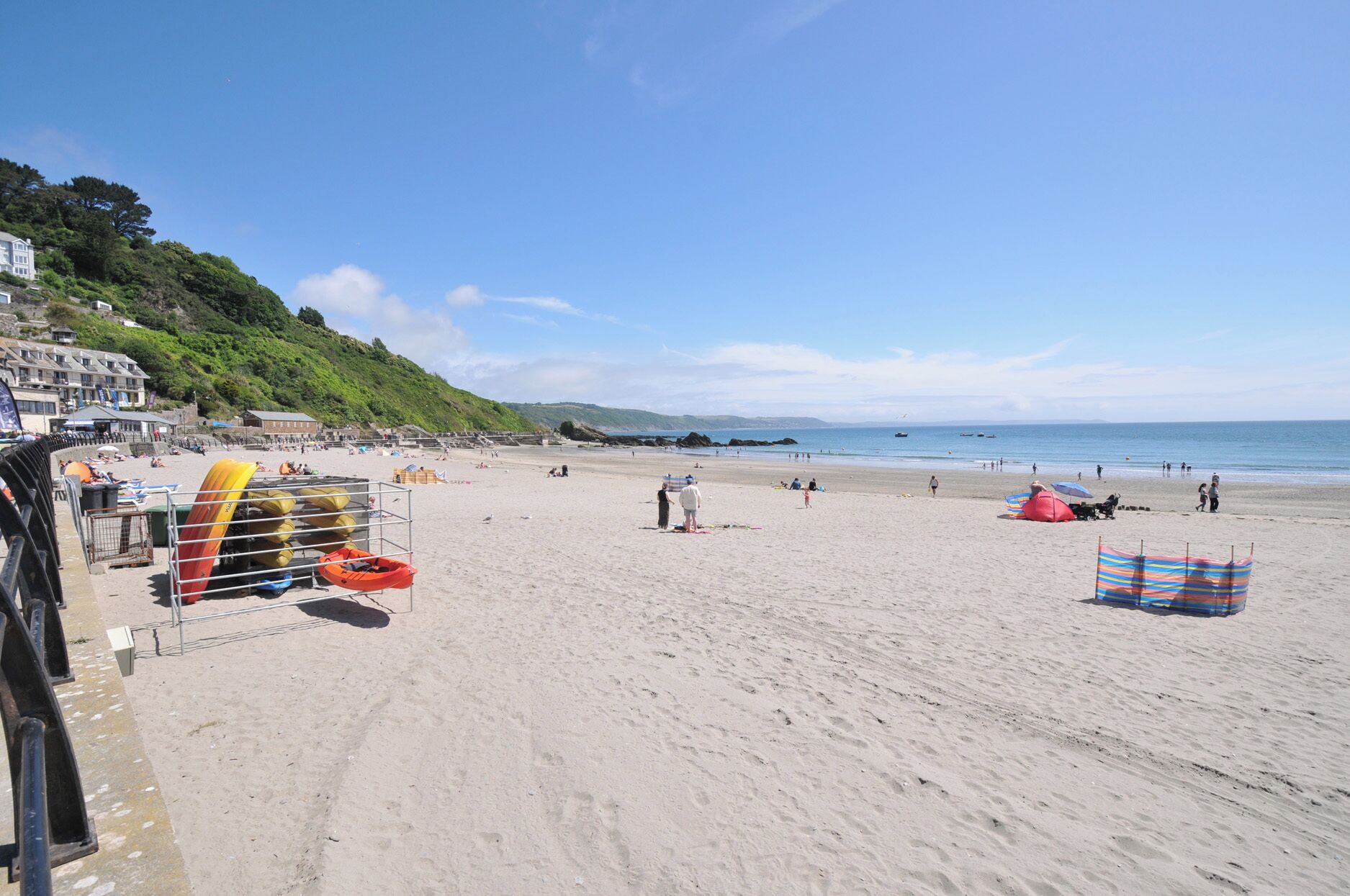 A beach with kayaks, umbrellas, and a building with steps leading down to the shore.