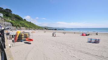 A beach with kayaks, umbrellas, and a building with steps leading down to the shore.