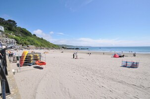 A beach with kayaks, umbrellas, and a building with steps leading down to the shore.