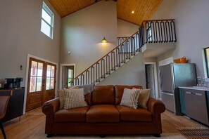 A spacious living area with a brown leather sofa, a wooden staircase, and a kitchen area. - Stay on the Wine Trail - Luxury 5-Acre Fredericksburg Private Retreat (Fredericksburg)
