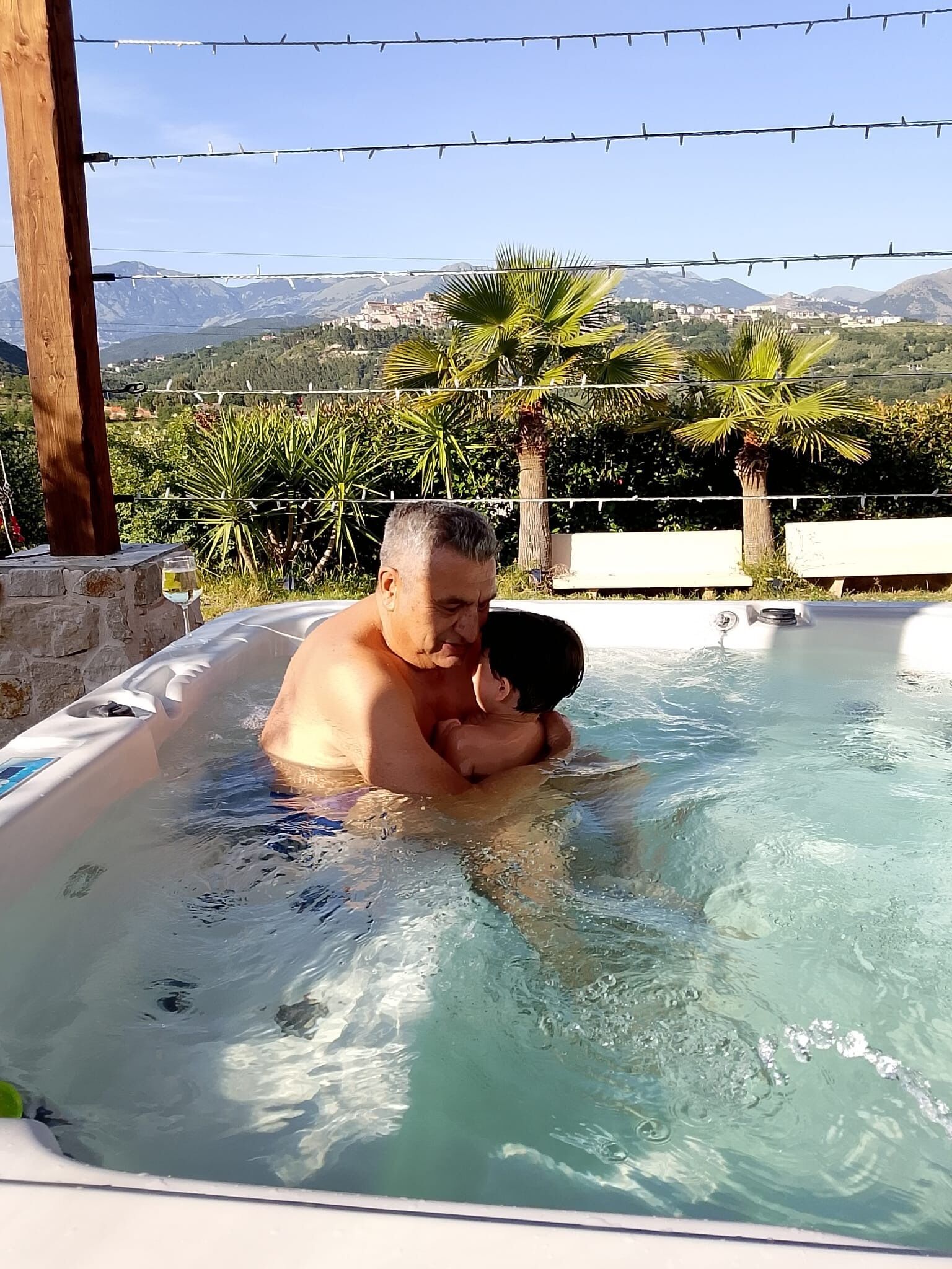 A man and a child in a hot tub with a mountainous landscape in the background.