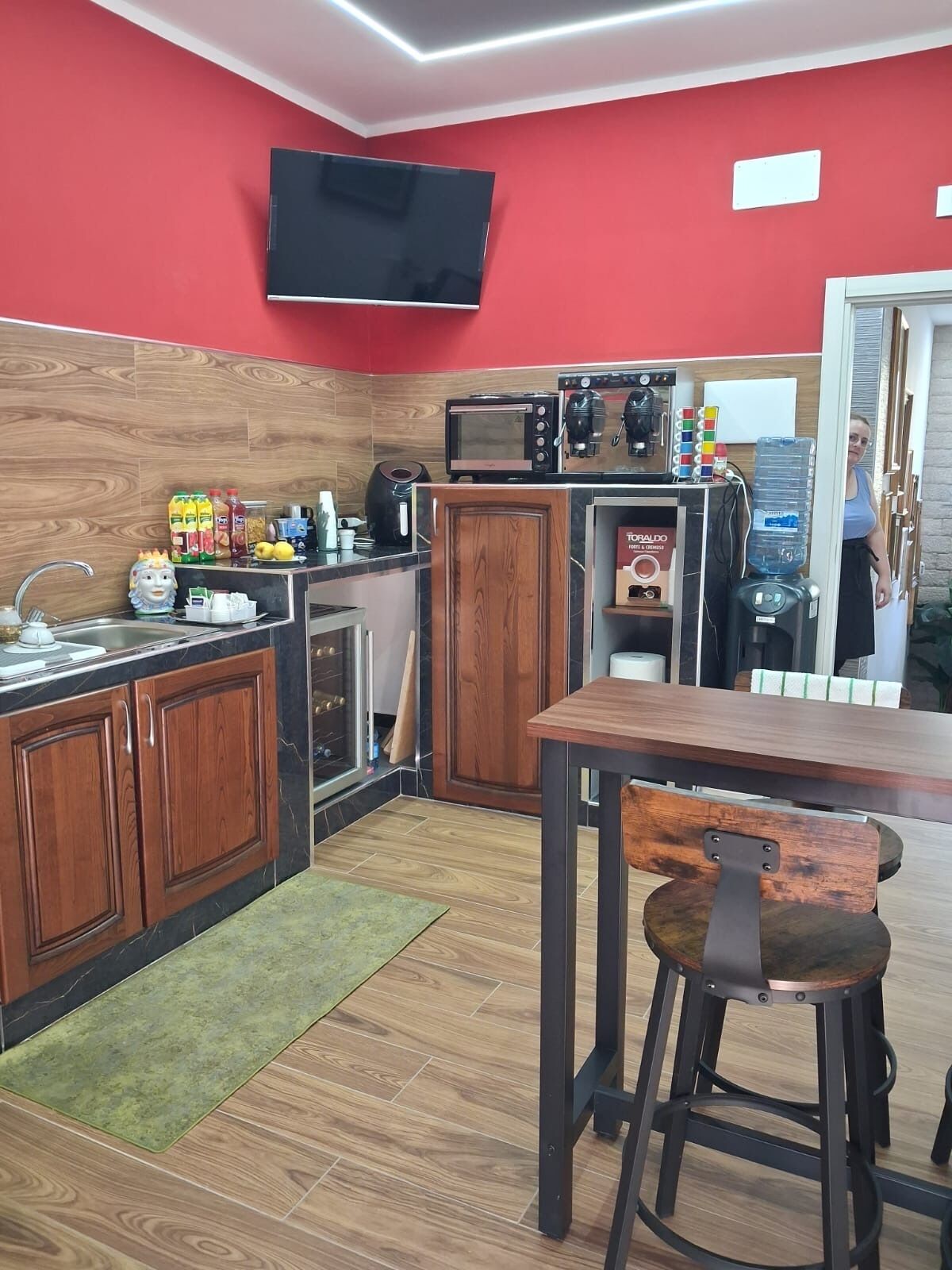 A compact kitchen with wooden cabinets, a microwave, a coffee machine, and a water dispenser.