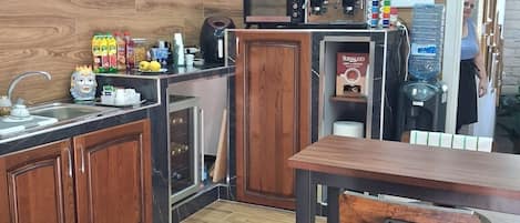 Cocina compacta con armarios de madera, microondas, cafetera y dispensador de agua.